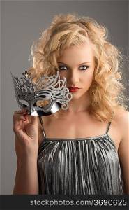 pretty blonde girl with curly hair takes one silver mask, she takes the mask with right hand and looks in to the lens