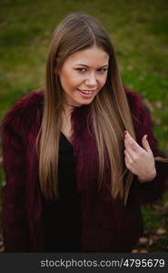 Pretty blonde girl with fur coat in the park at winter