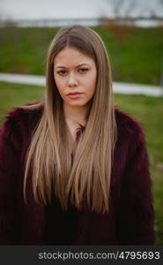 Pretty blonde girl with fur coat in the park at winter