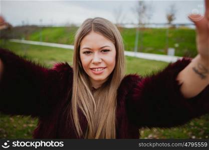 Pretty blonde girl with fur coat in the park making herself a photo