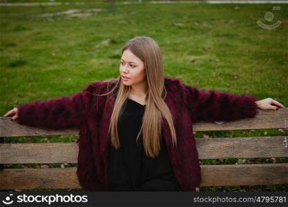 Pretty blonde girl with fur coat sittig in a bench in the park