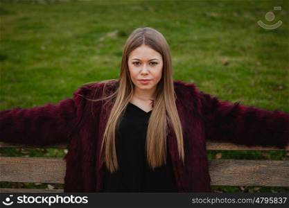 Pretty blonde girl with fur coat sittig in a bench in the park