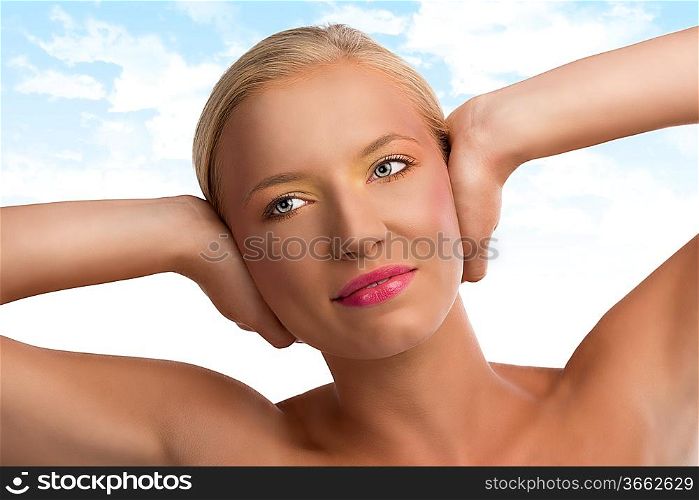 pretty blonde girl with naked shoulders and colored make-up, she looks at right and smiles and has both hands on the ears