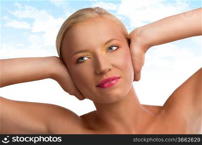 pretty blonde girl with naked shoulders and colored make-up, she looks at right and smiles and has both hands on the ears