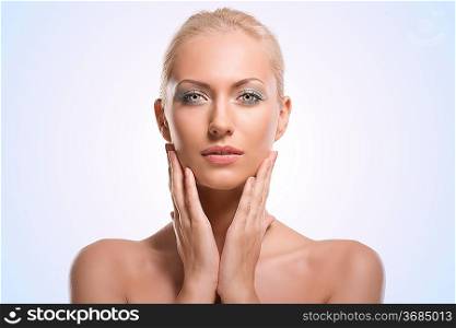 pretty blonde girl with naked shoulders, she touches her face with both hands and looks in to the lens with calm expression
