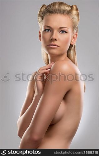 pretty blonde girl with naked torso and creative hair style. She is turned of three quarters at right and looks in to the lens