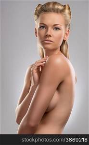 pretty blonde girl with naked torso and creative hair style. She is turned of three quarters at right and looks in to the lens