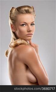 pretty blonde girl with naked torso and creative hair style, she is turned at right and she looks in to the lens