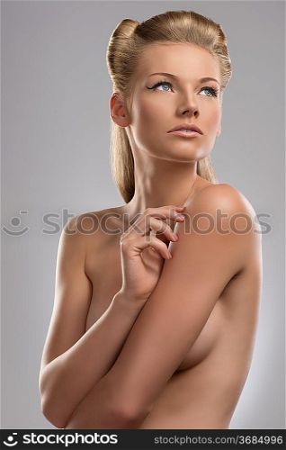 pretty blonde girl with naked torso and creative hair style, she is turned of three quarters at right and looks up at left