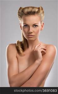 pretty blonde girl with naked torso and creative hair style, she looks in to the lens and her right hand is near the left shoulder