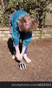 Pretty blonde haired girl making rows in the soil to plant with seeds