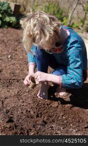Pretty blonde haired girl planting a seed in a pot