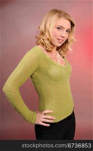 Pretty blonde teenager in a green knit sweater and black pants