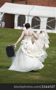 Pretty bride in wedding dress walking away from camera holding a blank board with space for copy