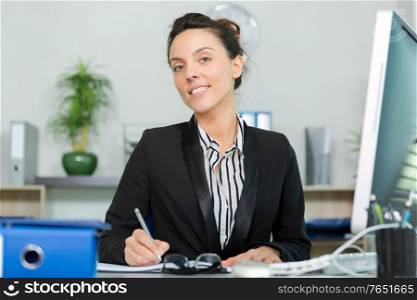 pretty brunette at office desk is writing down on paper