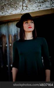 Pretty brunette girl in black with a stylish hat and a old wooden door of background