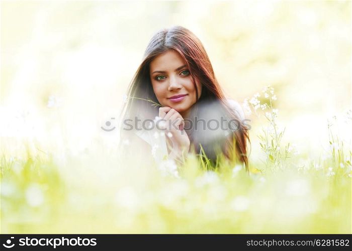 Pretty brunette girl laying on grass with white flowers around her
