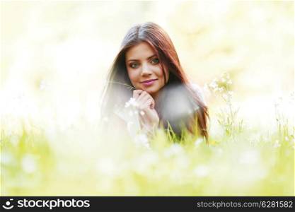 Pretty brunette girl laying on grass with white flowers around her
