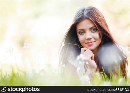 Pretty brunette girl laying on grass with white flowers around her. Pretty brunette girl laying on grass
