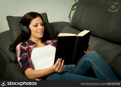 Pretty brunette girl reading and listening music on the sofa. Relax at home