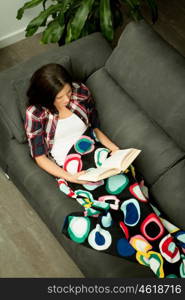 Pretty brunette girl reading on the sofa. Relax at home