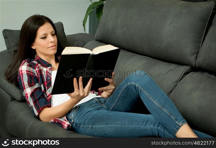 Pretty brunette girl reading on the sofa. Relax at home