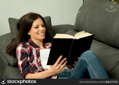 Pretty brunette girl reading on the sofa. Relax at home