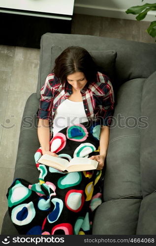 Pretty brunette girl reading on the sofa. Relax at home