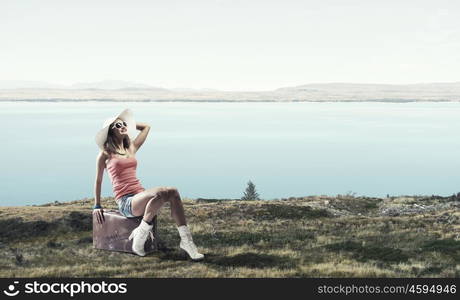 Pretty brunette retro hitchhiker. Traveler woman sits on her retro suitcase outdoors