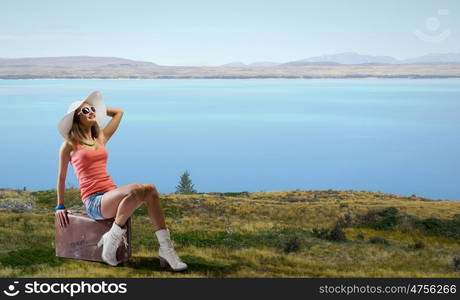 Pretty brunette retro hitchhiker. Traveler woman sits on her retro suitcase outdoors