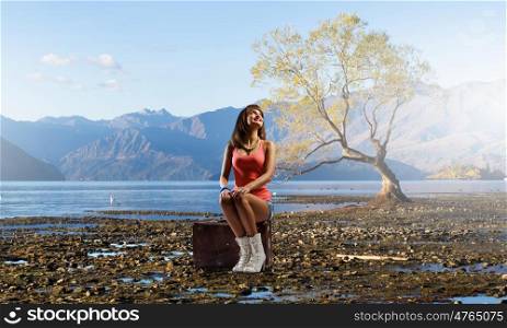 Pretty brunette retro hitchhiker. Traveler woman sits on her retro suitcase outdoors