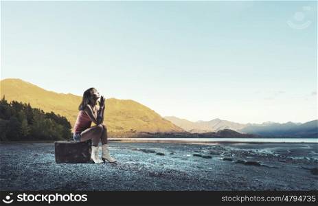 Pretty brunette retro hitchhiker. Traveler woman sits on her retro suitcase outdoors