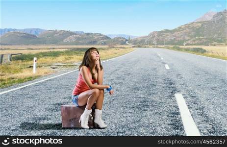 Pretty brunette retro hitchhiker. Traveler woman sits on retro suitcase and waiting for car