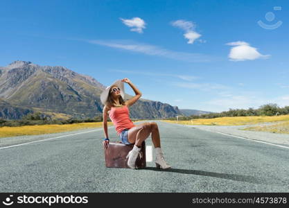 Pretty brunette retro hitchhiker. Traveler woman sits on retro suitcase and waiting for car
