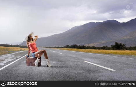 Pretty brunette retro hitchhiker. Traveler woman sits on retro suitcase and waiting for car