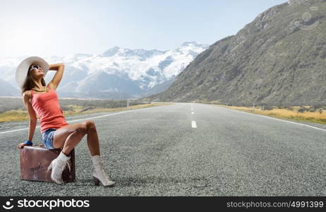 Pretty brunette retro hitchhiker. Traveler woman sits on retro suitcase and waiting for car