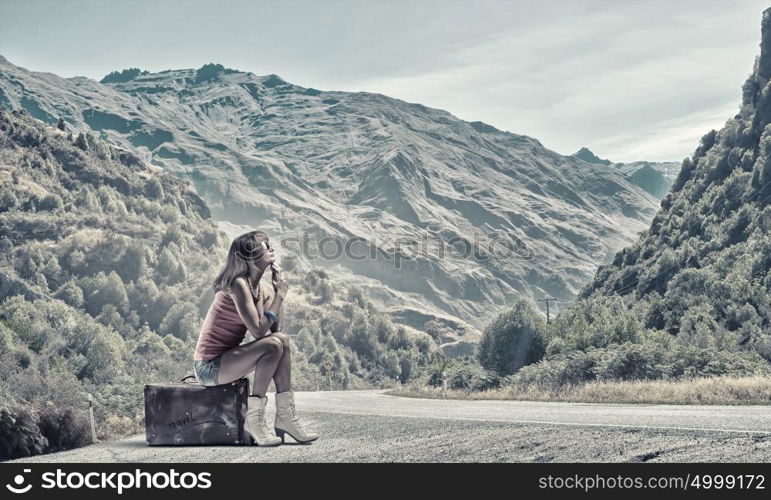 Pretty brunette retro hitchhiker. Traveler woman sits on retro suitcase and waiting for car