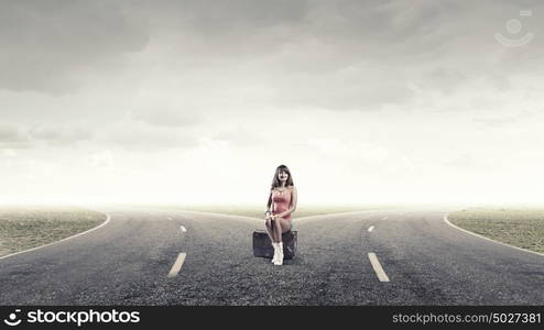 Pretty brunette retro hitchhiker. Traveler woman sits on retro suitcase and waiting for car