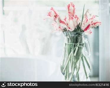 Pretty bunch of tulips in glass jug on white table at window. Flowers in interior design. Cozy home. Springtime