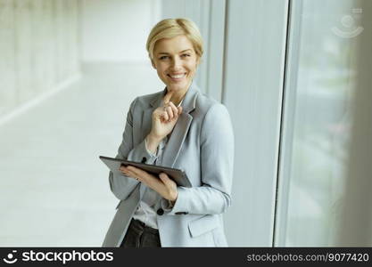 Pretty business woman standing with digital tablet in the office corridor