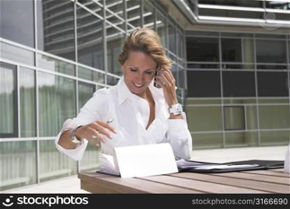 pretty businesswoman outdoors trying to control the documents while talking on the phone