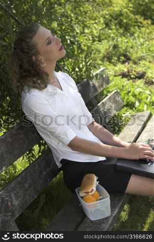 pretty businesswoman relaxing in the shade, with her laptop on her lap