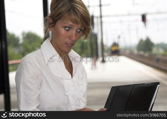 Pretty businesswoman sitting at the trainstation looking shocked at her notes (train is coming in the background)