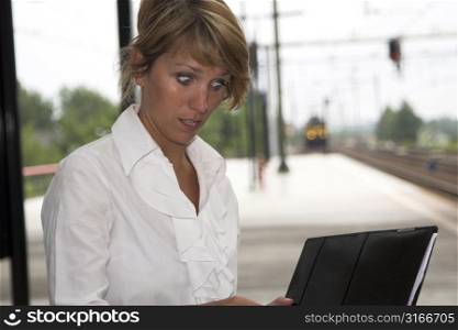 Pretty businesswoman sitting at the trainstation looking shocked at her notes (train is coming in the background)