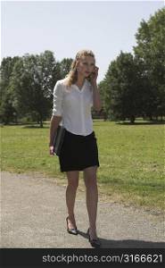 Pretty businesswoman walking in the park carrying a laptop and talking on the phone