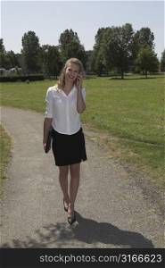 Pretty businesswoman walking in the park while talking on the phone