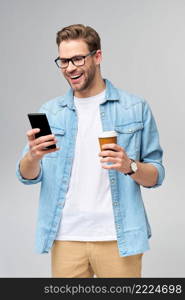 pretty casual man in blue jeans shirt holding his phone and cup of coffee to go standing over studio grey background.. pretty casual man in blue jeans shirt holding his phone and cup of coffee to go standing over studio grey background