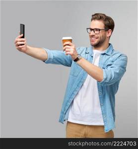 pretty casual man in blue jeans shirt holding his phone and cup of coffee to go standing over studio grey background.. pretty casual man in blue jeans shirt holding his phone and cup of coffee to go standing over studio grey background