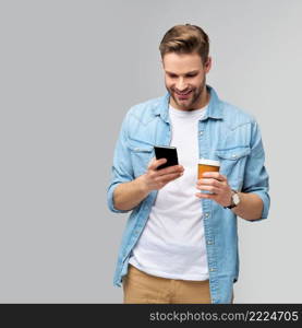 pretty casual man in blue jeans shirt holding his phone and cup of coffee to go standing over studio grey background.. pretty casual man in blue jeans shirt holding his phone and cup of coffee to go standing over studio grey background