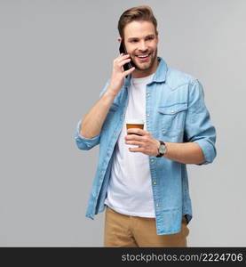 pretty casual man in blue jeans shirt holding his phone and cup of coffee to go standing over studio grey background.. pretty casual man in blue jeans shirt holding his phone and cup of coffee to go standing over studio grey background